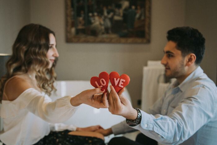 A couple holds red heart decor with text, representing sneaky scams in relationships.