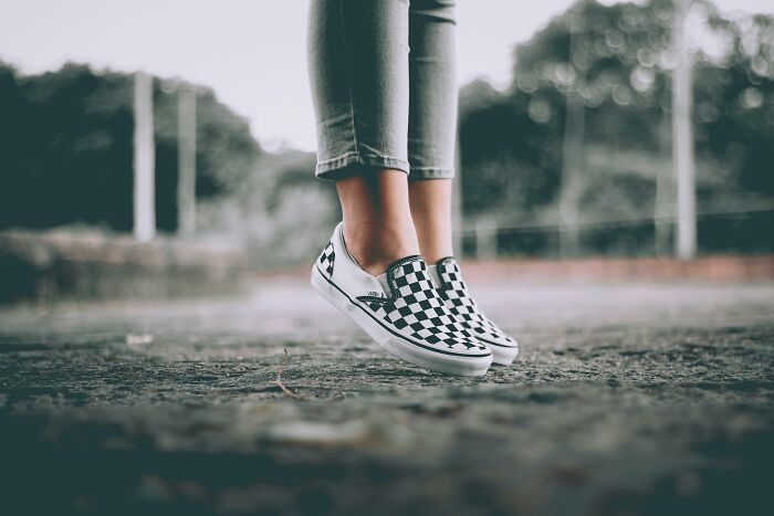 Checkered shoes on pavement, representing a tale of disruption, with a blurred nature background.