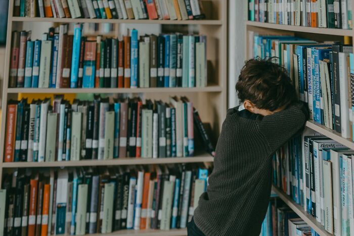 Child leaning against a bookshelf filled with historical books, reflecting on the dark side of history.