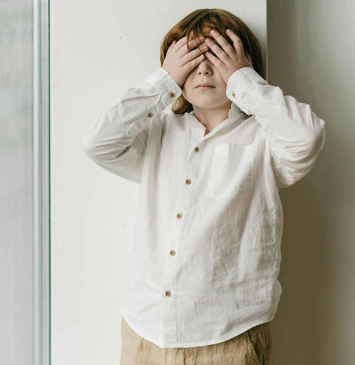 Child covering eyes, dressed in white, standing indoors, symbolizing red flag moments at weddings.