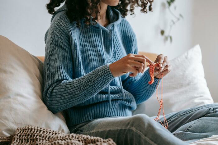 Person in a blue sweater knitting on a couch, highlighting work misconceptions.