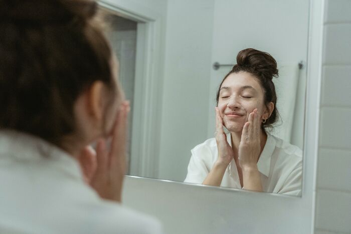 Person smiling while washing face in the mirror, representing self-care against stereotypes.
