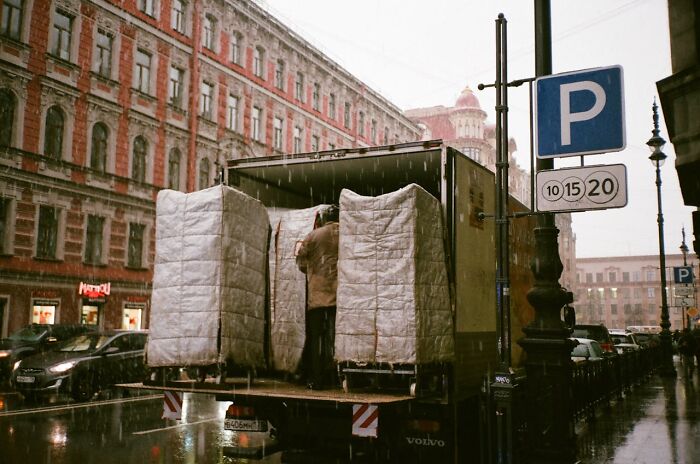 Man standing in truck under rain, surrounded by large items on a busy street. Worst job interview scene.