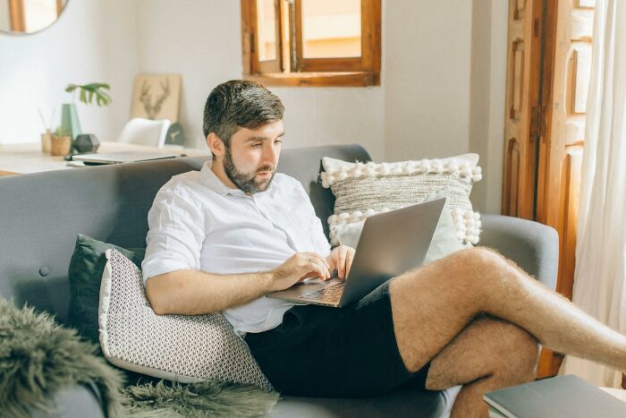 Man sitting on a sofa using a laptop, appearing focused, representing an online tale of frustration.