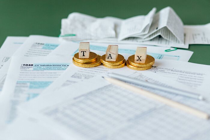 Tax forms with coins spelling "TAX" on wooden blocks, highlighting potential scams.