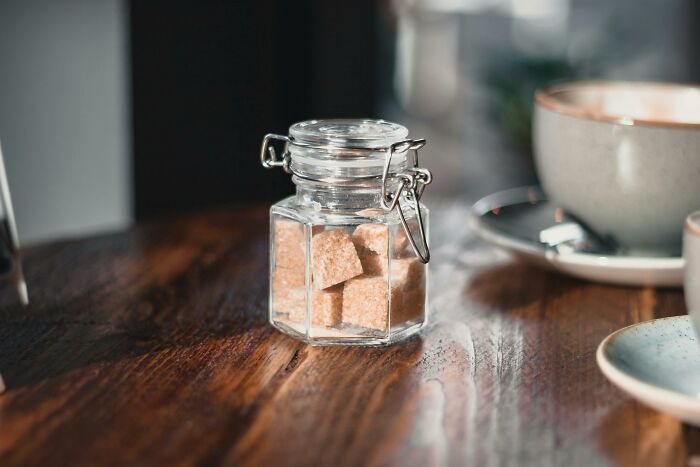 A jar of sugar cubes on a wooden table, next to a ceramic cup, related to wild theories people swear by.