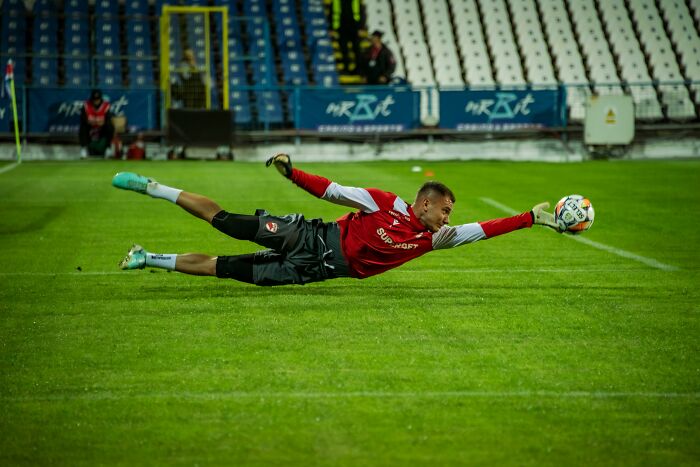 Goalkeeper diving to catch a soccer ball on the green field during a match.