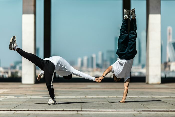 Two people doing handstands while holding hands in an urban outdoor setting.