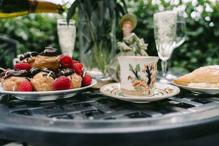 Wedding nightmare: outdoor table setting with pastries, a teacup, and champagne flutes, overshadowed by a doll centerpiece.