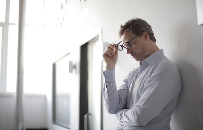 Man in thoughtful pose, wearing glasses and a light shirt, in a modern office setting, representing therapists' judgment.