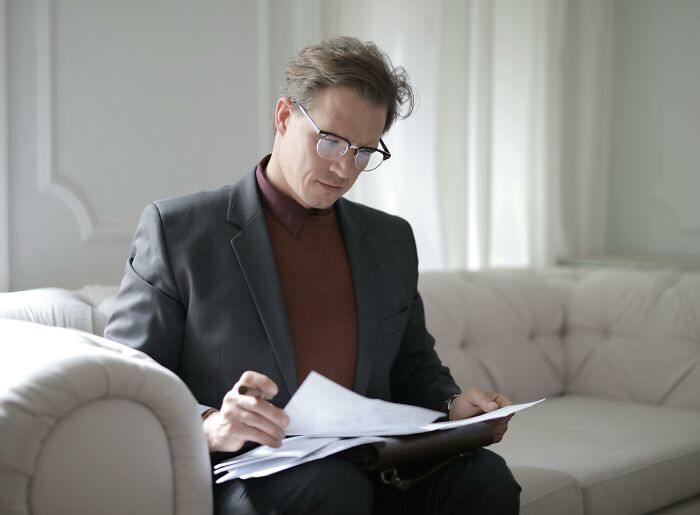 Man in glasses and a suit pondering documents, showcasing signs of intelligence.