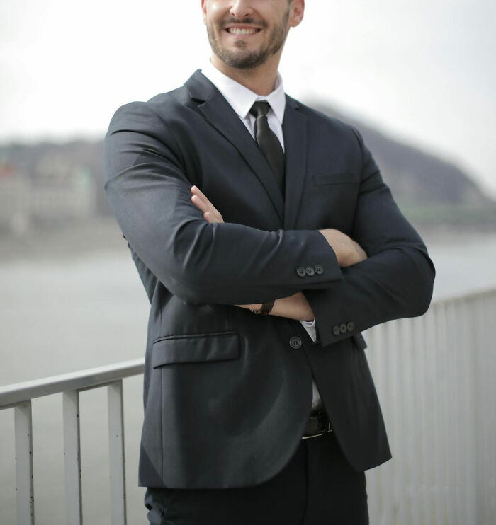 Man in a suit with arms crossed, smiling outdoors, representing worst bonus stories shared by people.