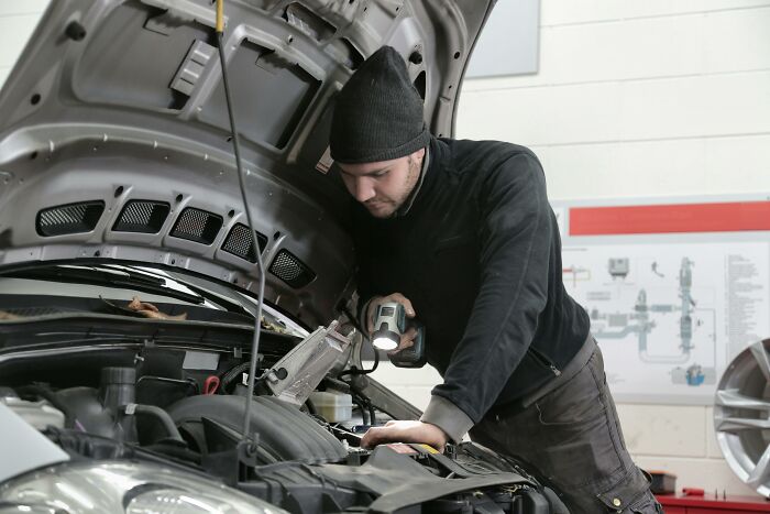 Mechanic working under a car hood, addressing common job misconceptions.