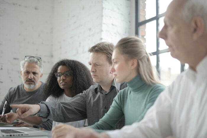 Office workers gathered around a table, engaging in a discussion with focused expressions.