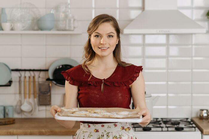 A woman in a maroon top, holding a tray of baked goods in a kitchen, representing unsettling stories theme.