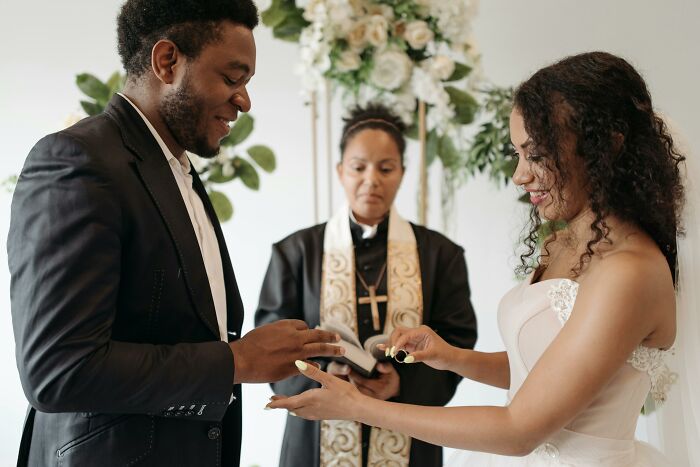 Bride and groom exchanging rings at a wedding ceremony, with an officiant observing.