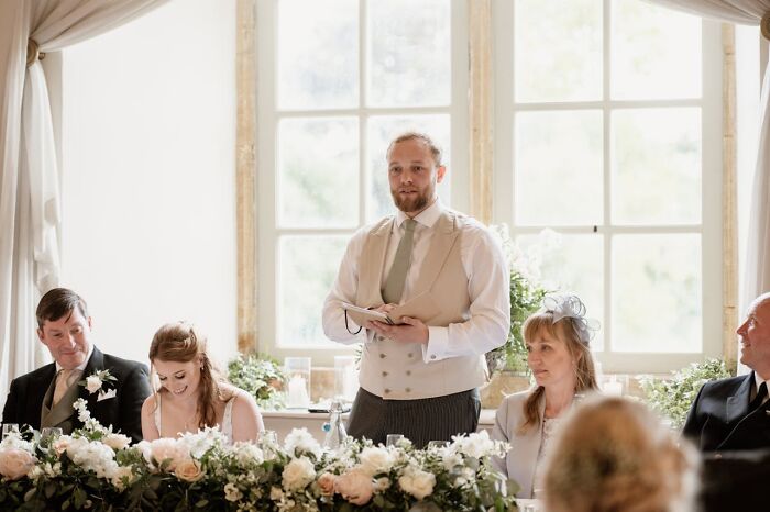 Man giving speech at a wedding, guests seated at decorated table, highlighting a potential wedding red flag moment.