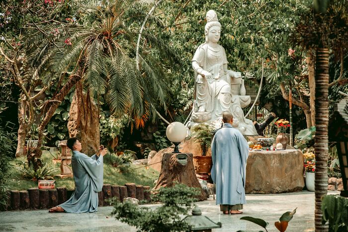 Monks in traditional attire performing a ceremony in front of a large Asian statue amidst lush greenery. Monks in traditional attire performing a ceremony in front of a large Asian statue amidst lush greenery.
