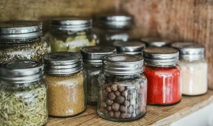 A variety of spices in jars on a wooden shelf, illustrating frugal hacks like making my own bread.