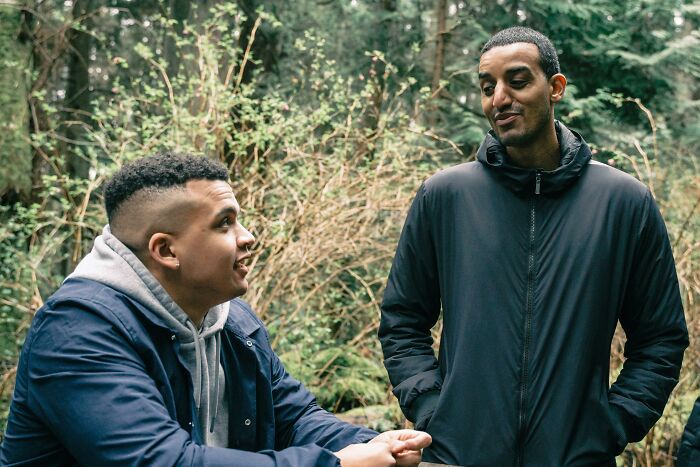 Two people in a forest setting having a conversation, exploring dating experiences across genders.