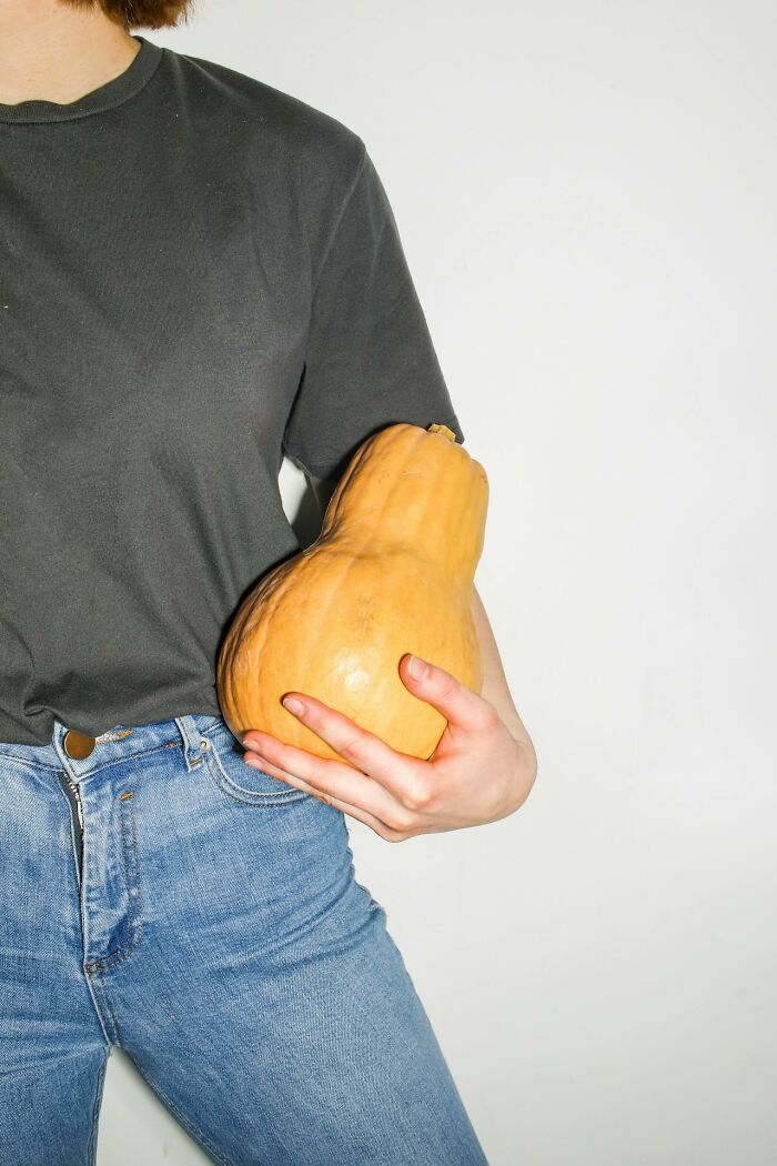 A person in jeans holding a large, oddly shaped squash against a white background.