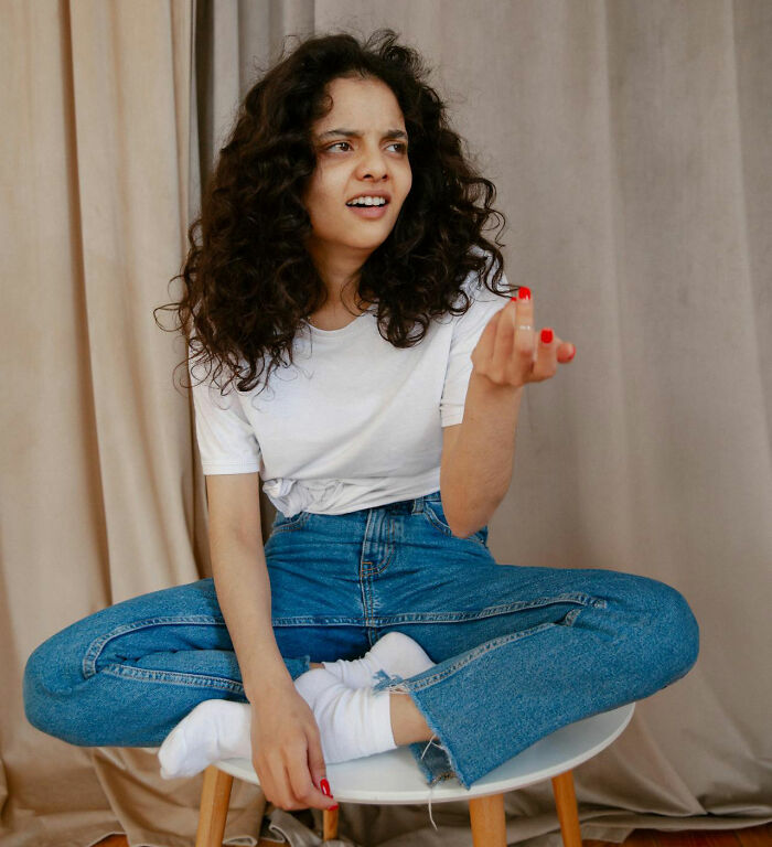 Woman sitting cross-legged in jeans and a white shirt, possibly reacting to being fired by her boss.
