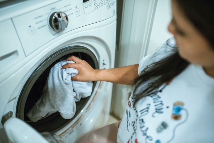 Person placing a gray shirt into a washing machine, considering frugal hacks and homemade alternatives.