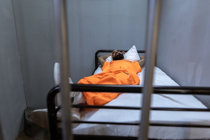 Person in orange jumpsuit lying on a bed behind bars, symbolizing a tough job interview experience.