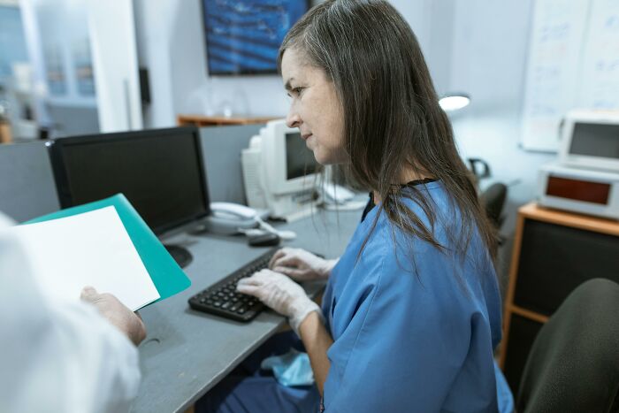 Woman in blue scrubs at a desk, typing on a keyboard, discussing outcomes of a "useless" degree.