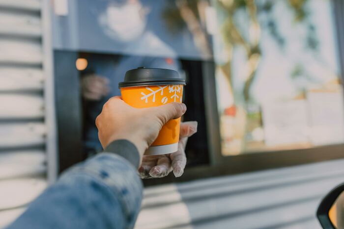 Hand receiving a coffee cup through a drive-thru window, focusing on customer service interaction.