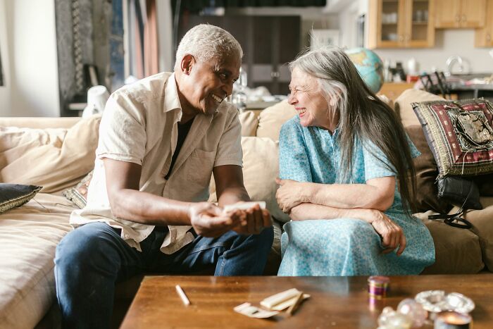 Elderly man and woman smiling and talking on a sofa, reflecting on life and sharing regrets.