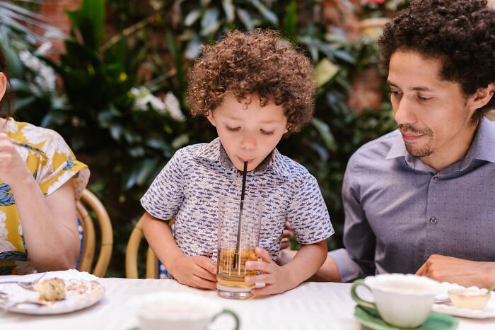 Child sipping juice with a man at a wedding reception.