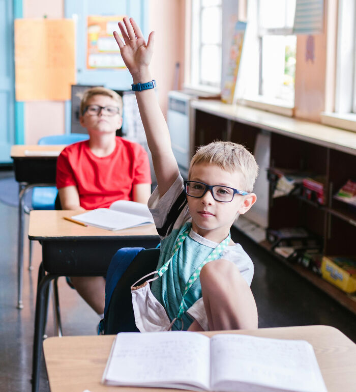 Student with glasses raises hand in class, questioning historical facts taught by school teachers.