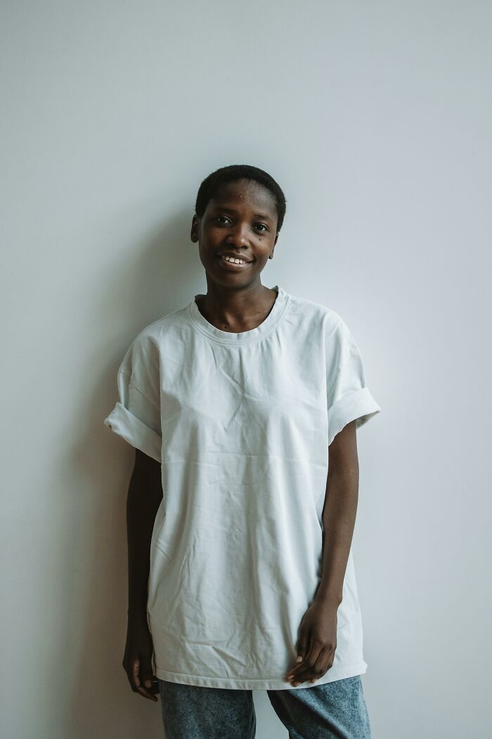 Person wearing a white shirt, embodying authentic beauty standards, standing against a plain wall.