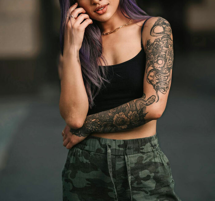 Woman with arm tattoos, wearing a black top and camouflage pants.