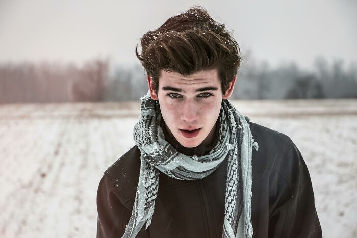 Young man in snowy field, wearing a scarf and jacket, symbolizing unforgettable heartfelt compliments.