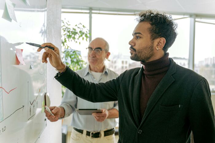 Man writing on a whiteboard, possibly showcasing signs of intelligence, as another person observes attentively.