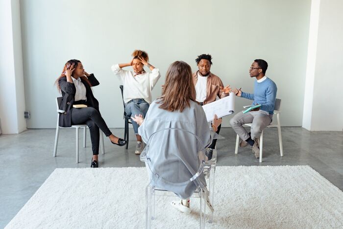 Therapist leading a group therapy session with four participants discussing animatedly in a bright room.