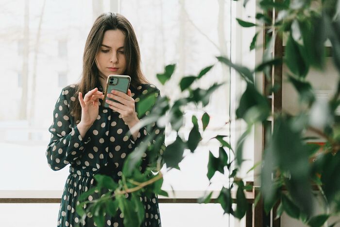 Woman in a polka dot dress using a smartphone, surrounded by indoor plants, exploring misunderstood 'healthy' trends.