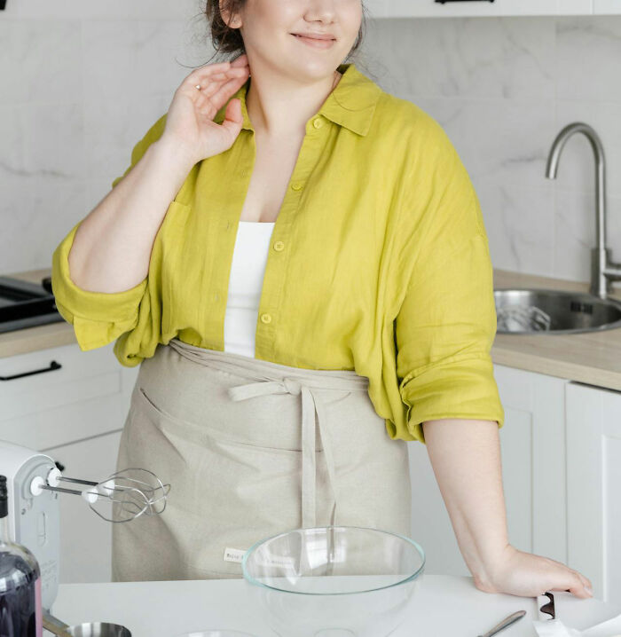 Woman in kitchen wearing a lime green shirt and beige apron, standing next to a mixer.