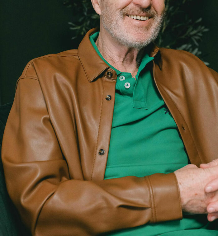 Man in a green shirt and brown jacket, smiling slightly, representing wedding red flag discussions.