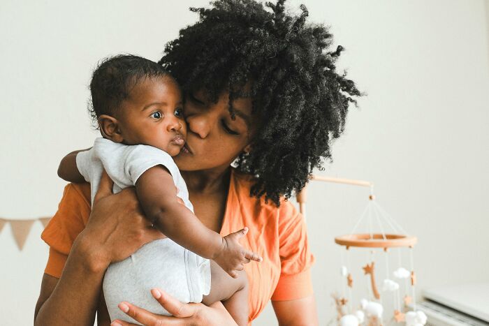 Woman holding and kissing a baby in a cozy nursery setting.