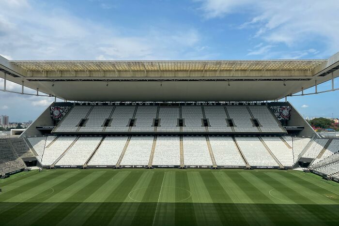 Empty soccer stadium with pristine field and white seats under a bright sky, showcasing one of the cathedrals of soccer.