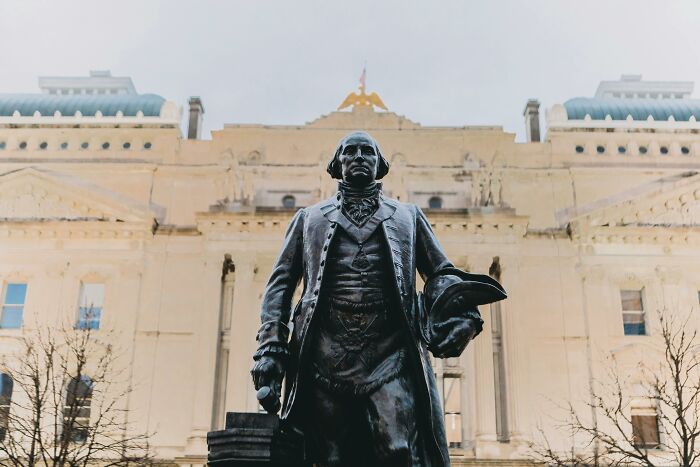 Historical statue of a man in front of a grand building, highlighting school-taught facts that are now questioned.