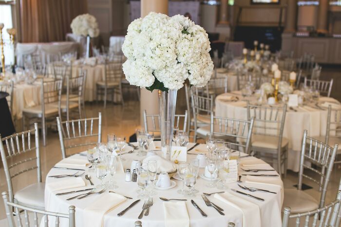 Elegant wedding reception setup with white floral centerpiece and silver chairs.