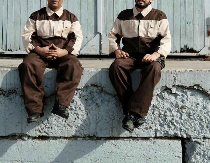 Two workers in brown uniforms sitting on a concrete ledge, possibly reflecting on abrupt firing experiences.