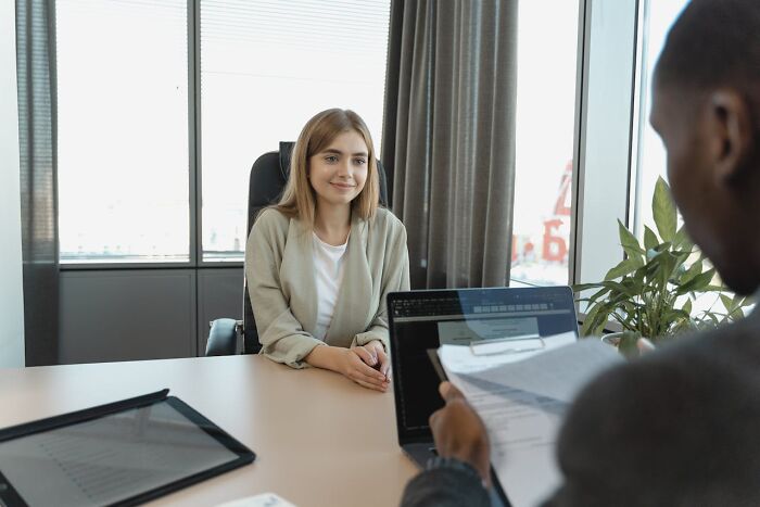 Candidate smiling in a job interview while the interviewer reviews documents in an office setting.