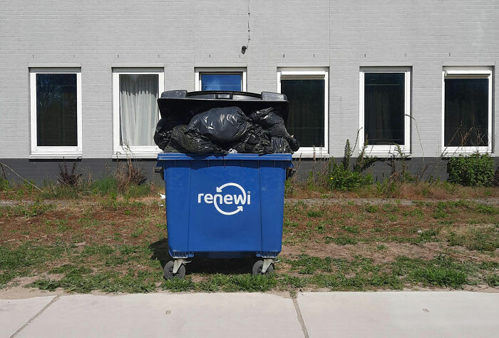 Blue dumpster overflowing with black garbage bags in front of a building, symbolizing harsh employee dismissals.