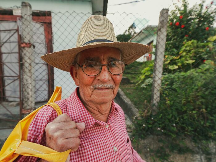 Elderly man in a straw hat and red shirt smiling while carrying a yellow bag, embodying unforgettable heartfelt compliments.