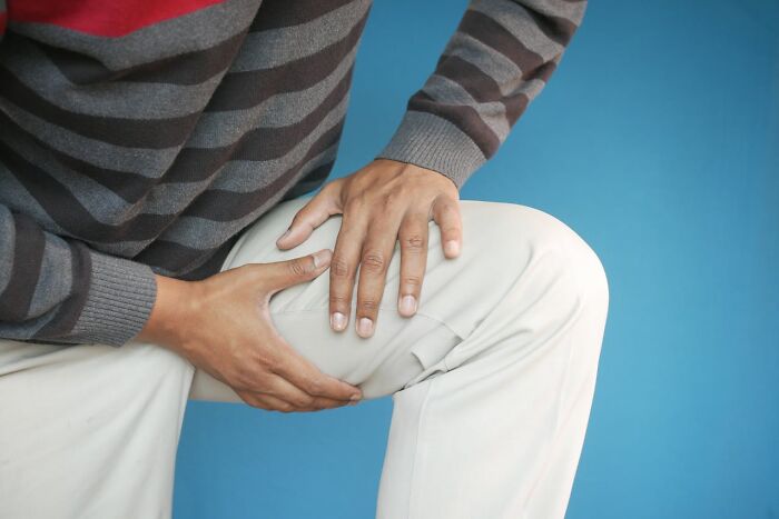 Person gripping their knee, symbolizing discomfort or pain, with a blue background.
